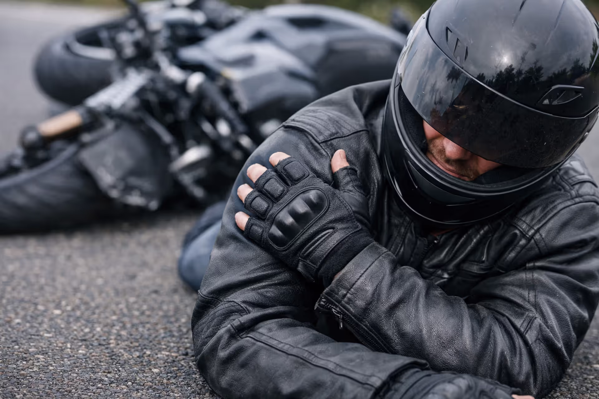 Motorcyclist on the ground after a crash clutching his injured shoulder with a fallen motorcycle in the background